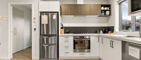 A modern kitchen with stainless steel appliances, white cabinetry, and a wooden upper shelf.