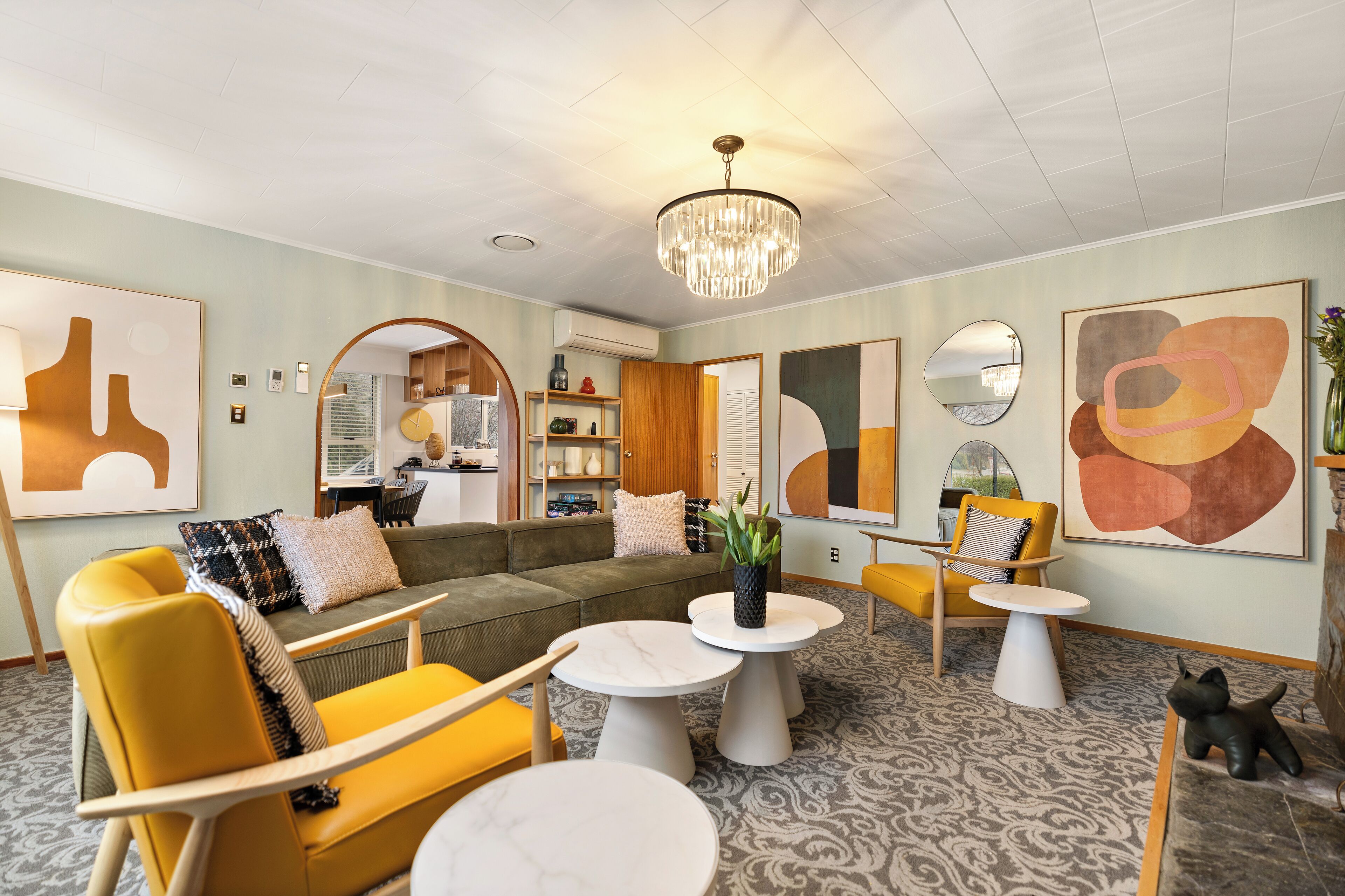 A modern living room with a sofa, yellow chairs, and round tables.