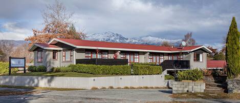 Un hotel con tejado rojo, un amplio camino de entrada y montañas al fondo.