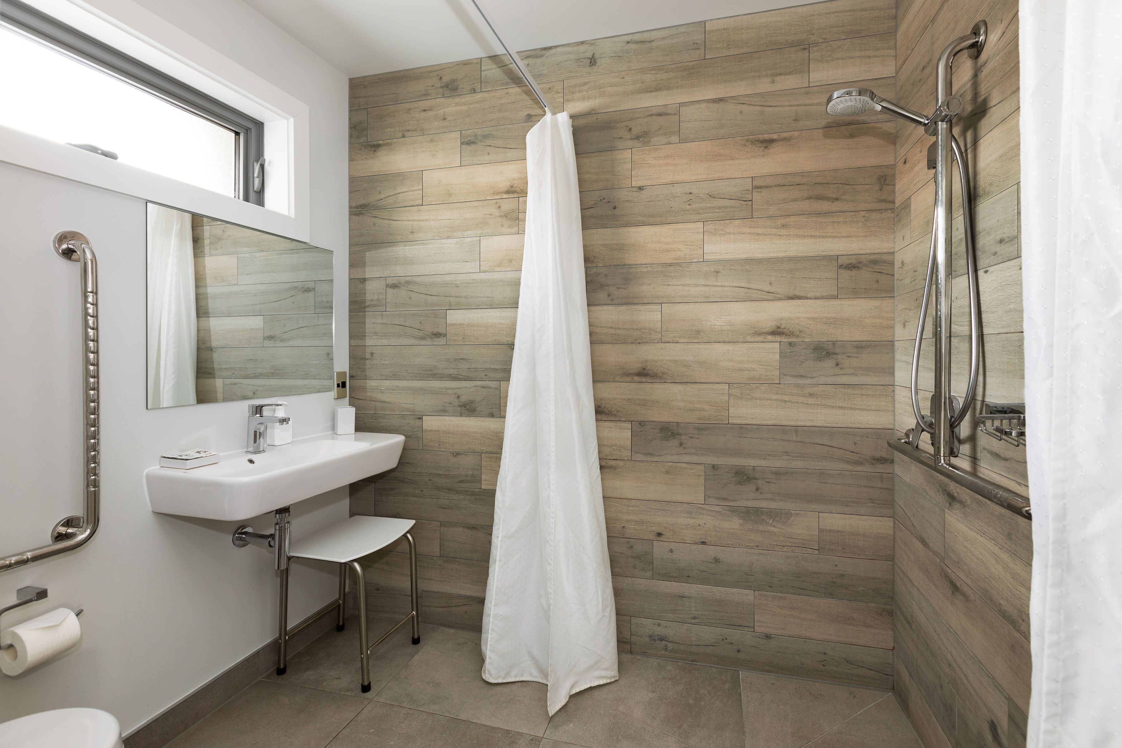 A modern bathroom with a wooden wall, a white sink, a mirror, and a shower with a curtain.