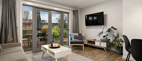 A modern living room with a sofa, a coffee table, a TV mounted on the wall, and a sliding glass door leading to an outdoor area.