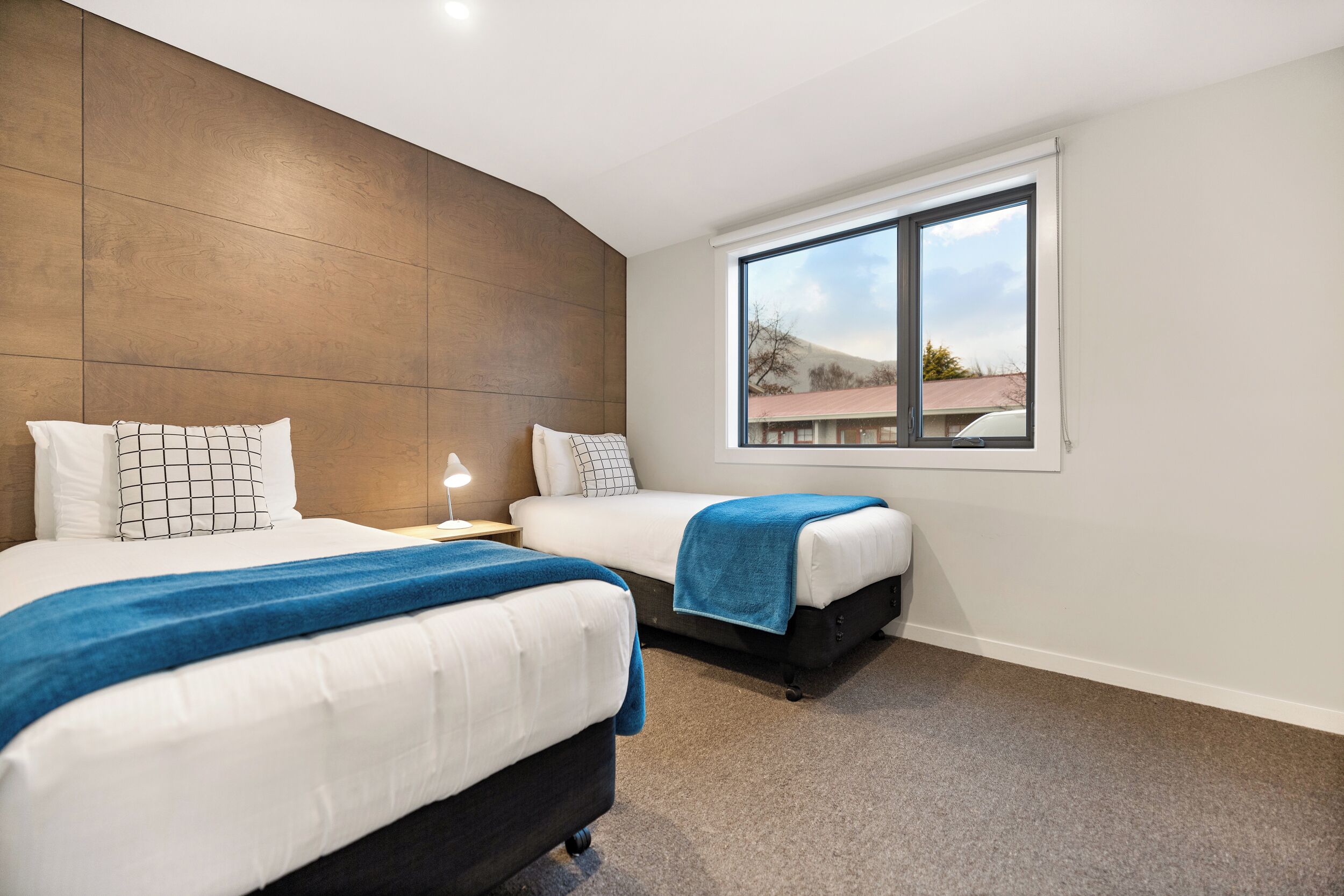 Quarto de hotel moderno com duas camas, uma janela grande e vista para o exterior.