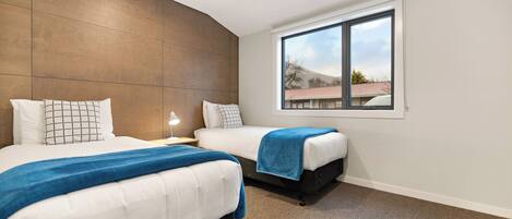 A modern hotel room with two beds, a large window, and a view of the outside.