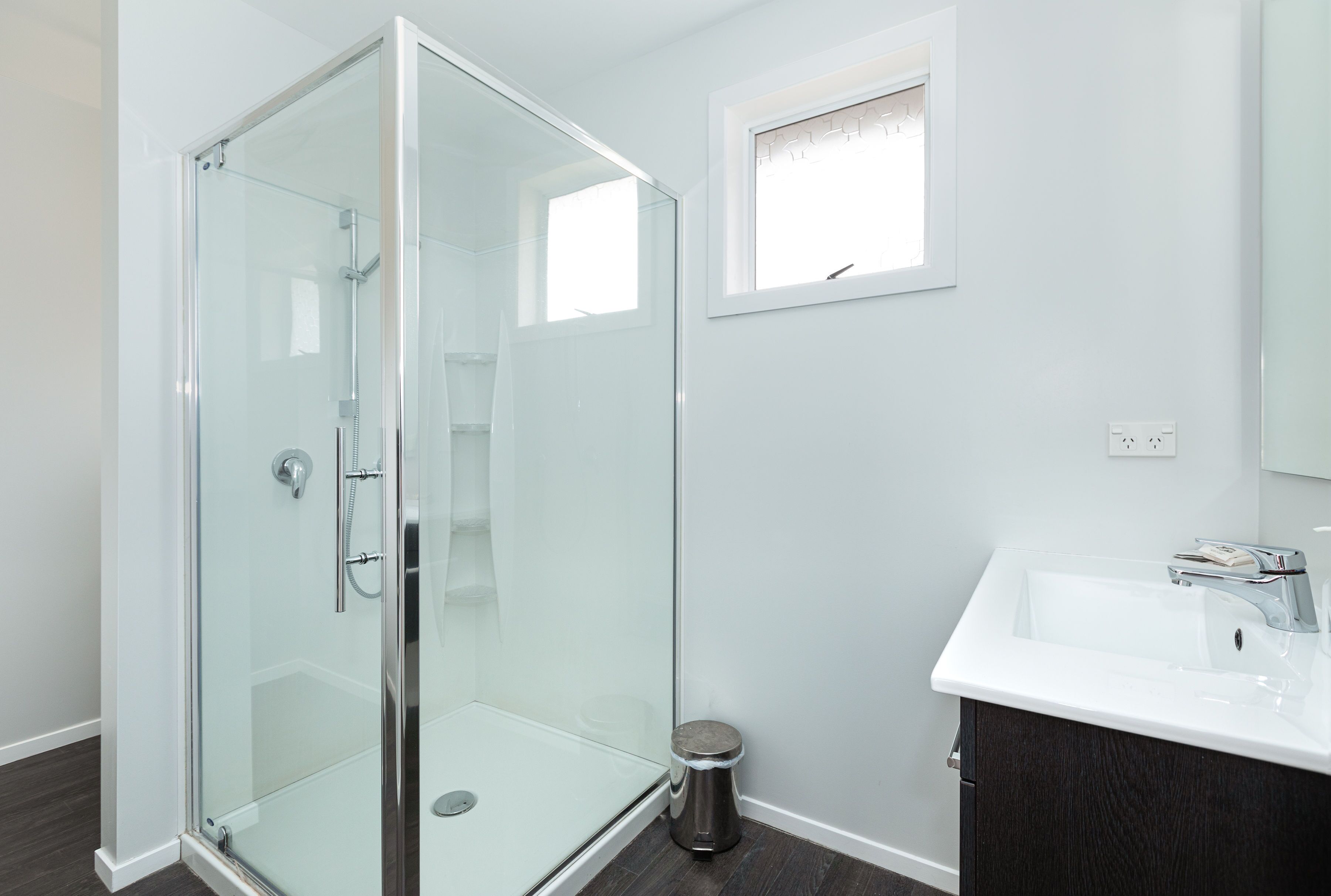Une salle de bain moderne avec une douche à parois de verre, un lavabo blanc et des meubles en bois foncé.
