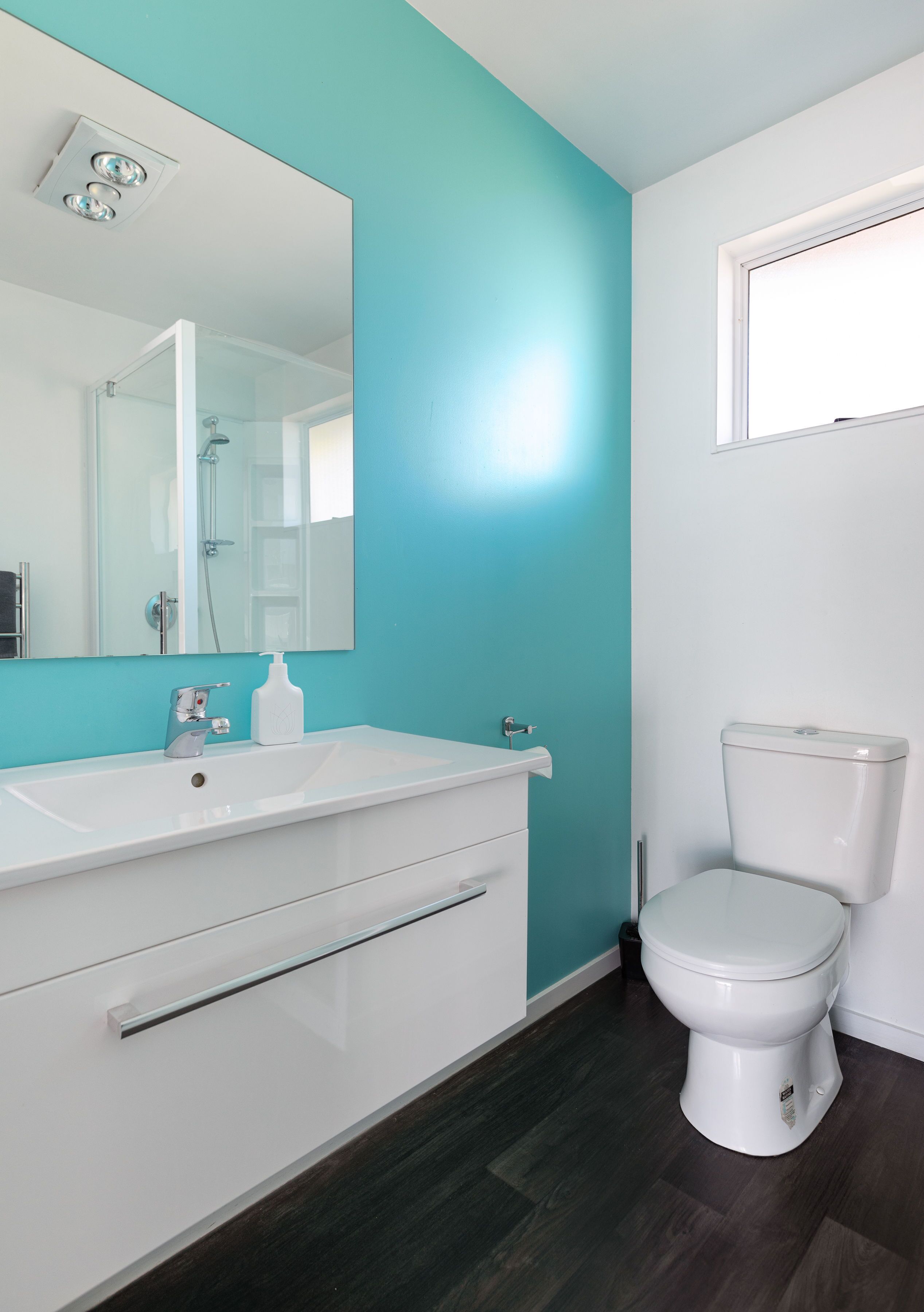 A bathroom with a white sink, a mirror, a toilet, and teal walls.