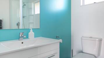 Un baño con lavamanos blanco, espejo, inodoro y paredes color turquesa.