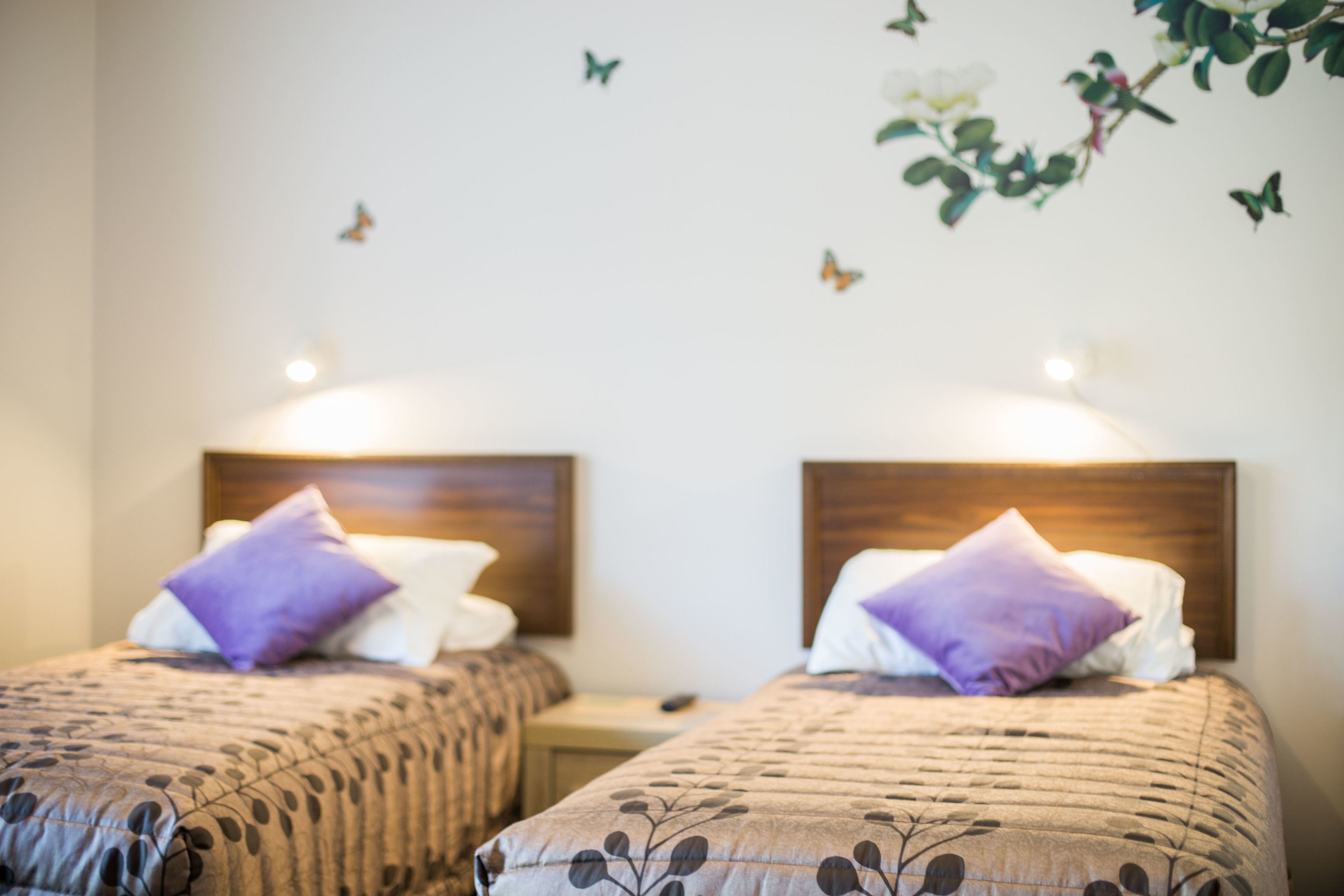 A hotel room with two beds, each with a wooden headboard and a purple pillow.