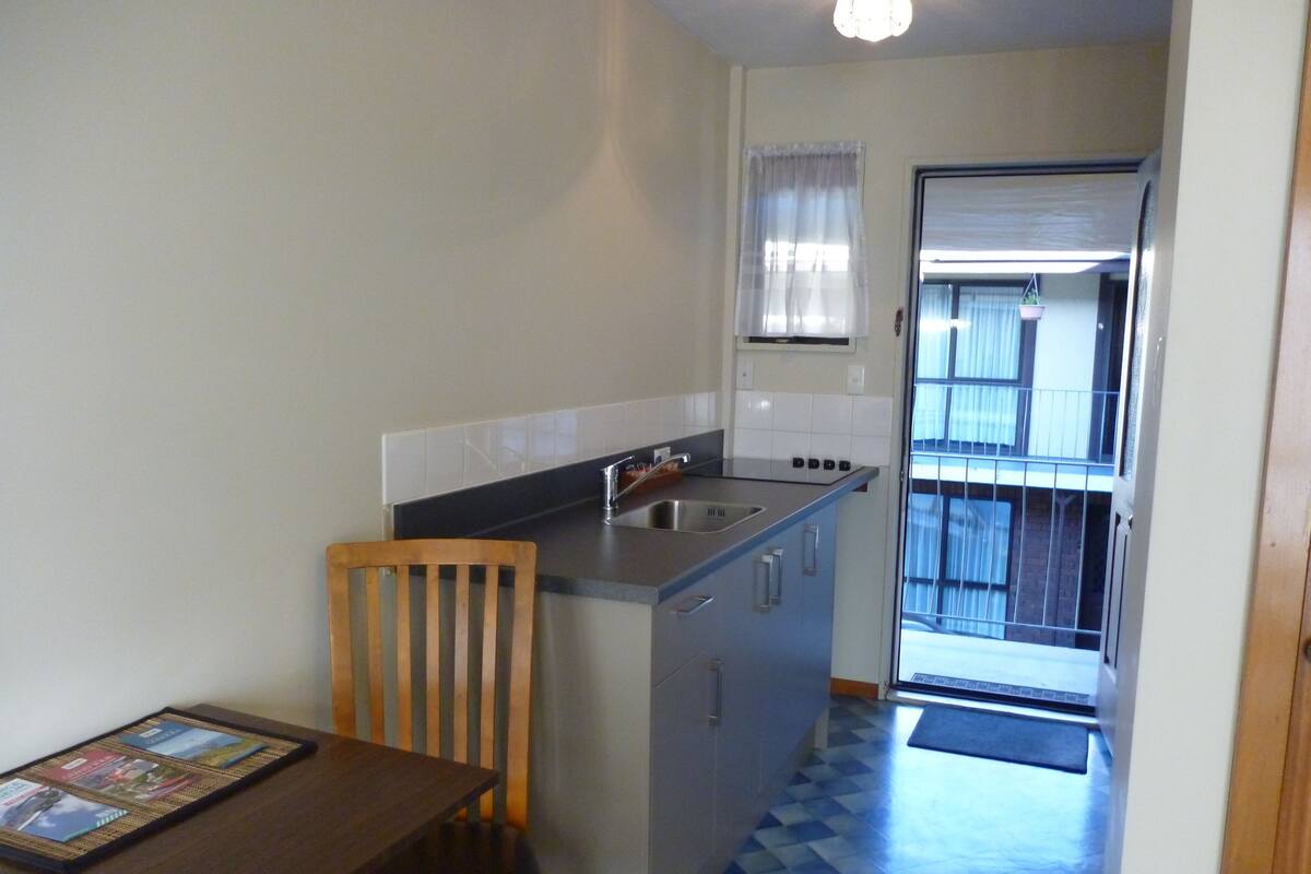 Une cuisine compacte comprenant une table à manger et une chaise, un petit évier et une fenêtre avec des rideaux.