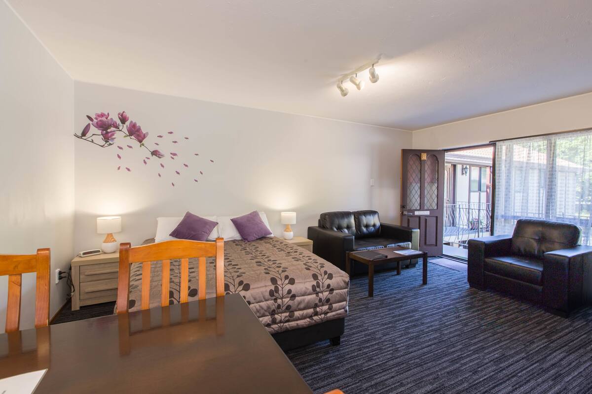 Une chambre d’hôtel avec un lit, deux chaises, une table, un canapé et une grande fenêtre.