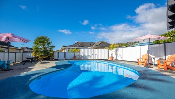 Una piscina con cubierta azul, rodeada por una valla blanca y dos sombrillas a rayas rojas y blancas.