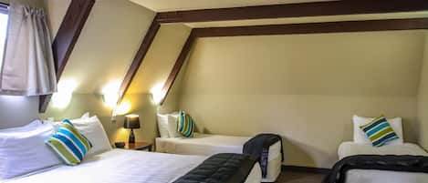 A hotel room with two beds, a nightstand with a lamp, and a window with curtains.