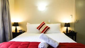 Una habitación de hotel con una cama bien hecha, dos mesitas de noche con lámparas, un reloj y una puerta.