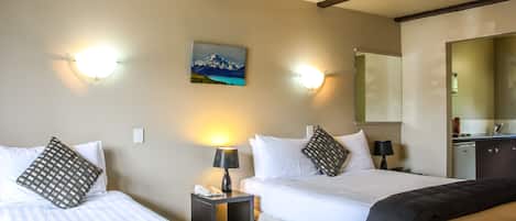 A hotel room with two beds, a painting of a mountain landscape, and a small kitchenette.