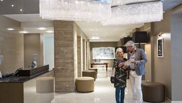 A modern lobby with a reception desk, seating areas, and a large chandelier.