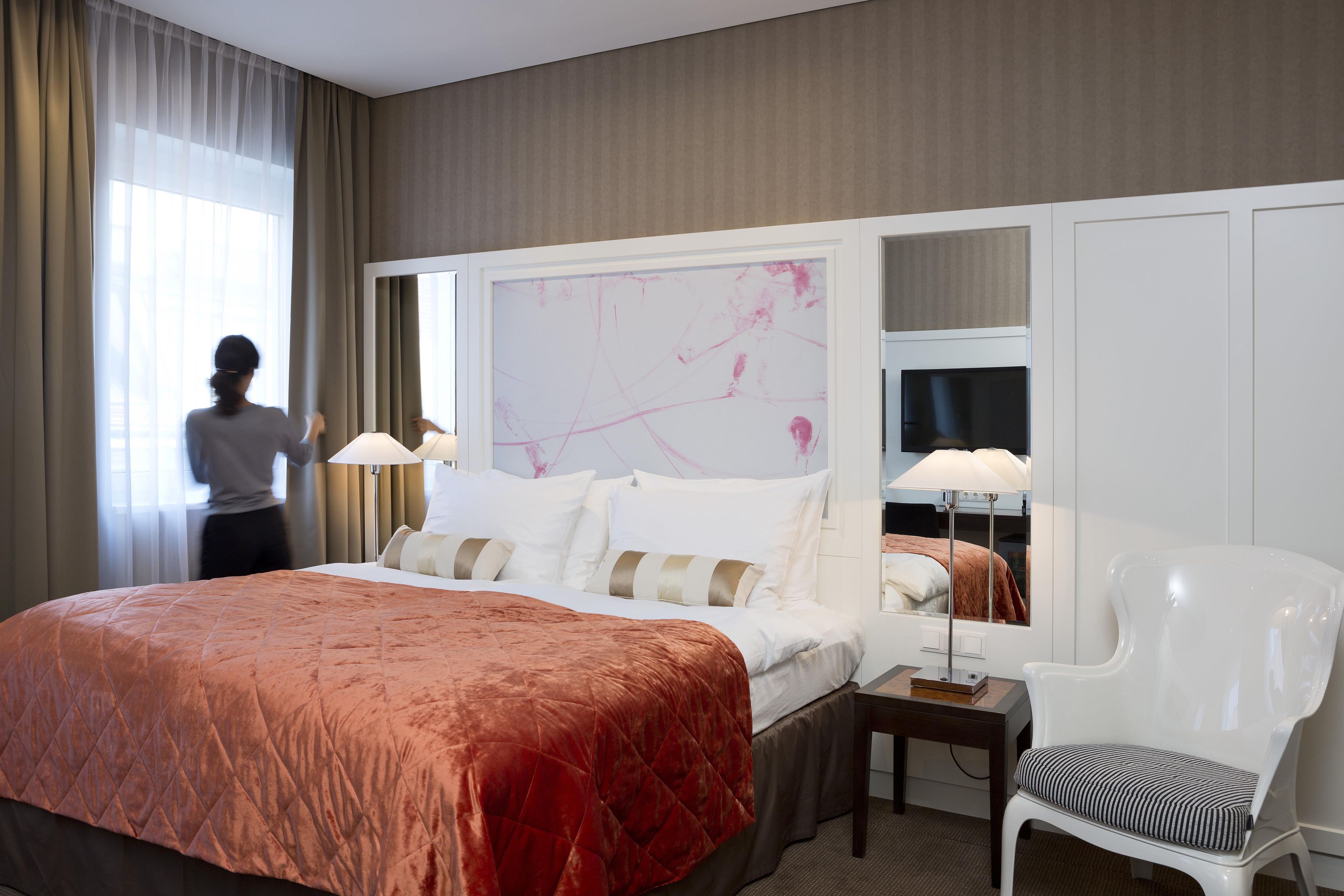 A hotel room with a large bed, a bedside table with a lamp, a chair, and a mirror.