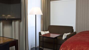 Una habitación de hotel con una televisión de pantalla plana, una lámpara, un sofá y una cama.
