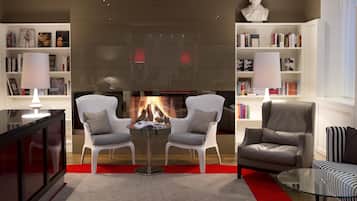 Een moderne woonkamer met een open haard, twee fauteuils, een bank en een glazen salontafel.