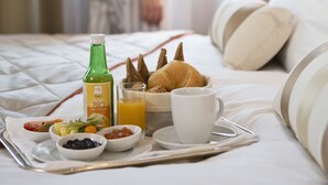 A breakfast tray with croissants, fruit, and a bottle of juice on a bed with a lamp and pillows. - The Harmonie Vienna, BW Premier Collection (Vienna)