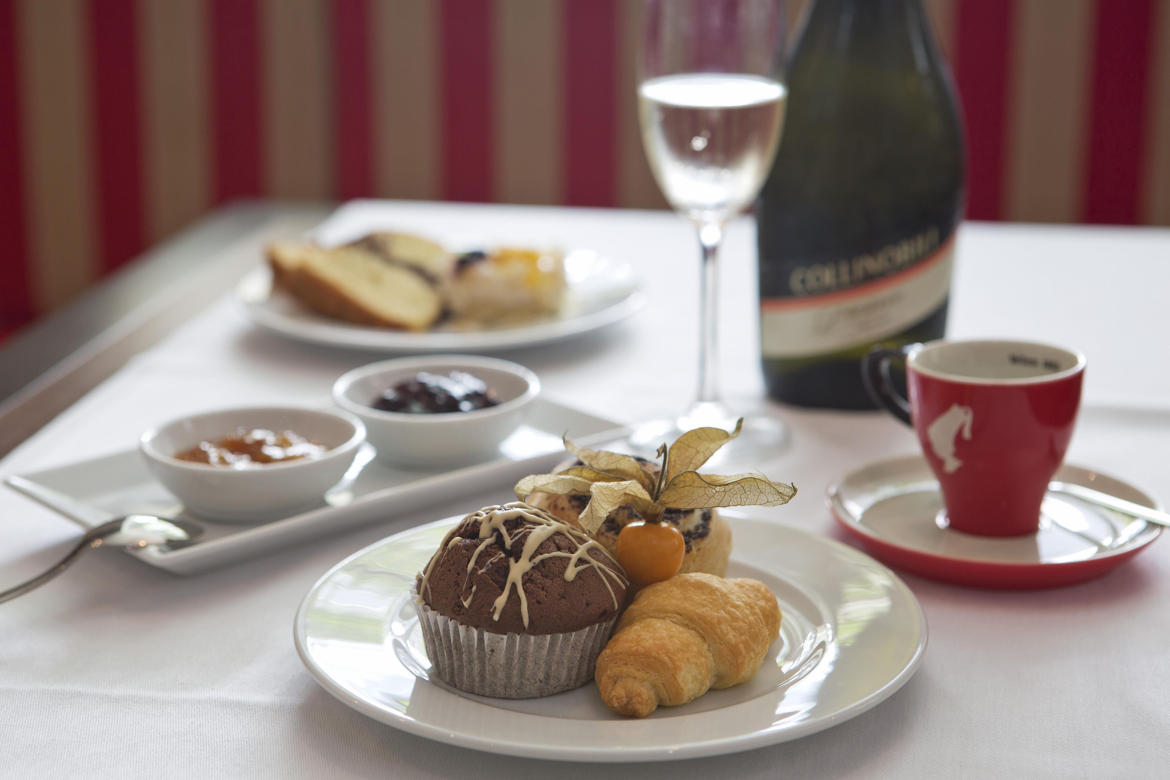 Un desayuno con una bandeja de pasteles, una copa de vino y una taza de café.