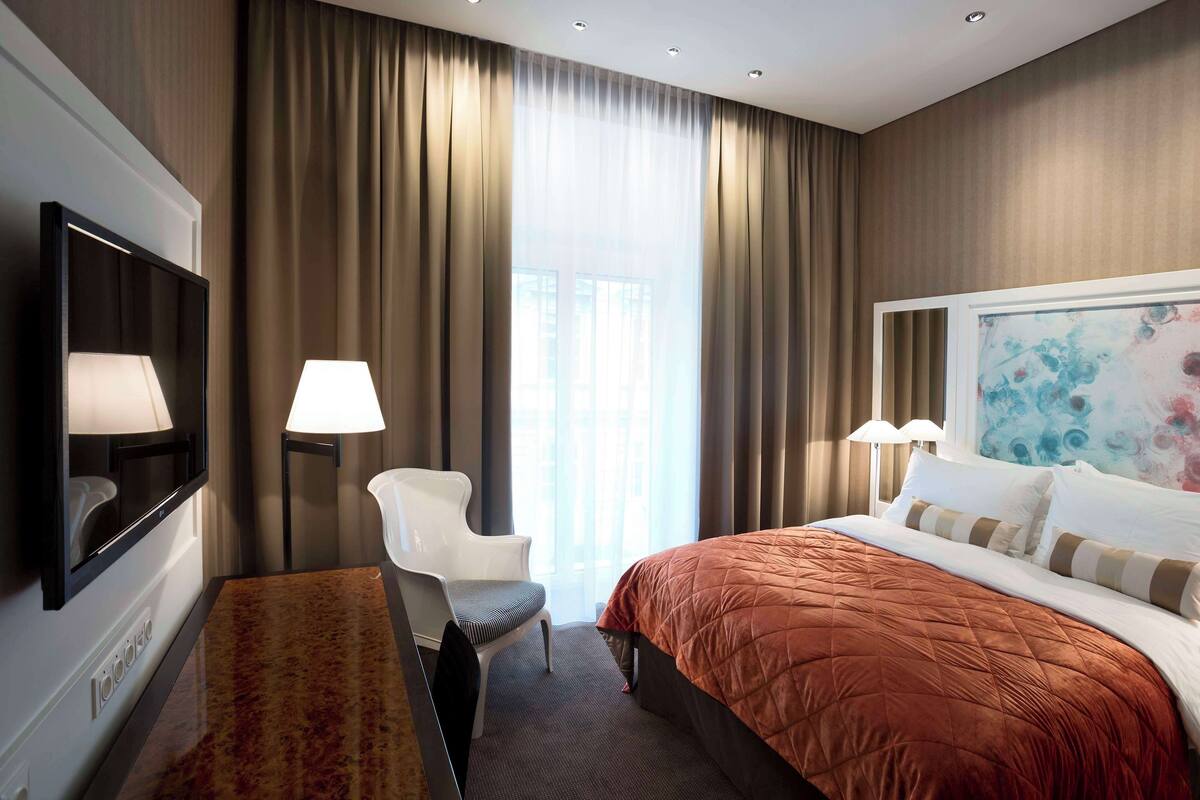 A hotel room with a large bed, a chair, a desk, and a TV.