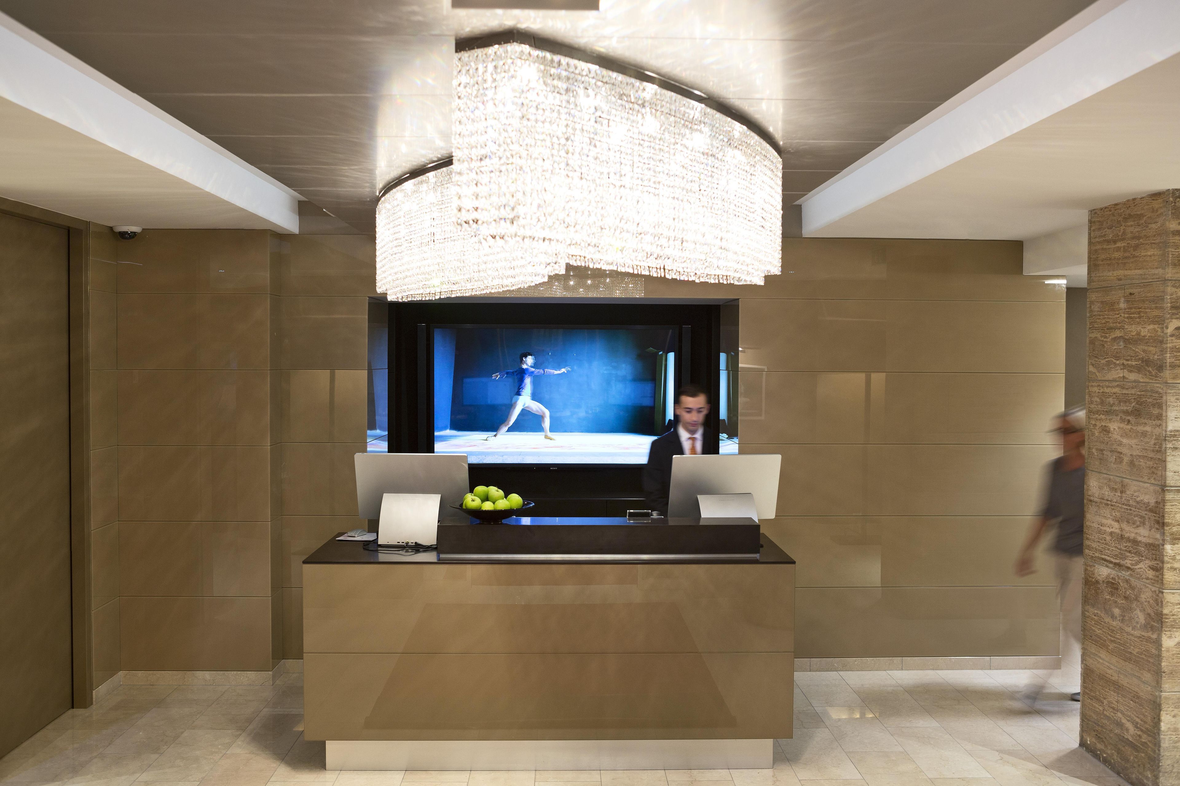 A modern reception area with a large flat-screen TV, a bowl of apples, and a laptop on a desk.