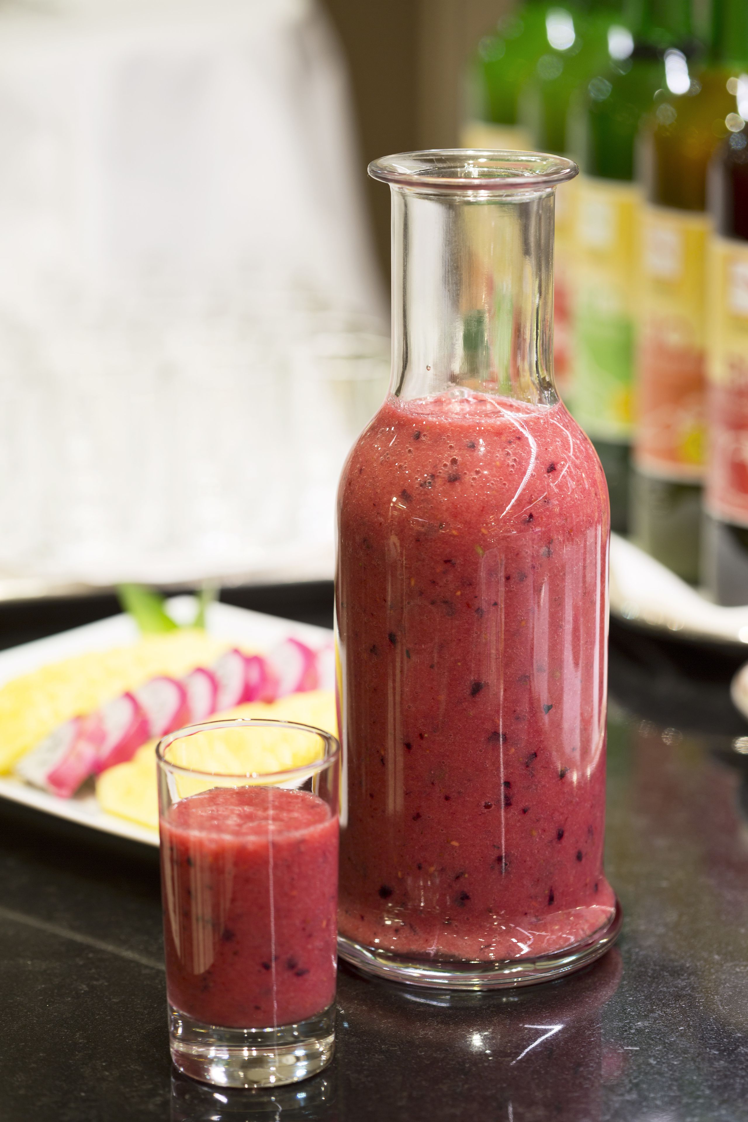 A glass bottle and a glass of a red smoothie on a table.
