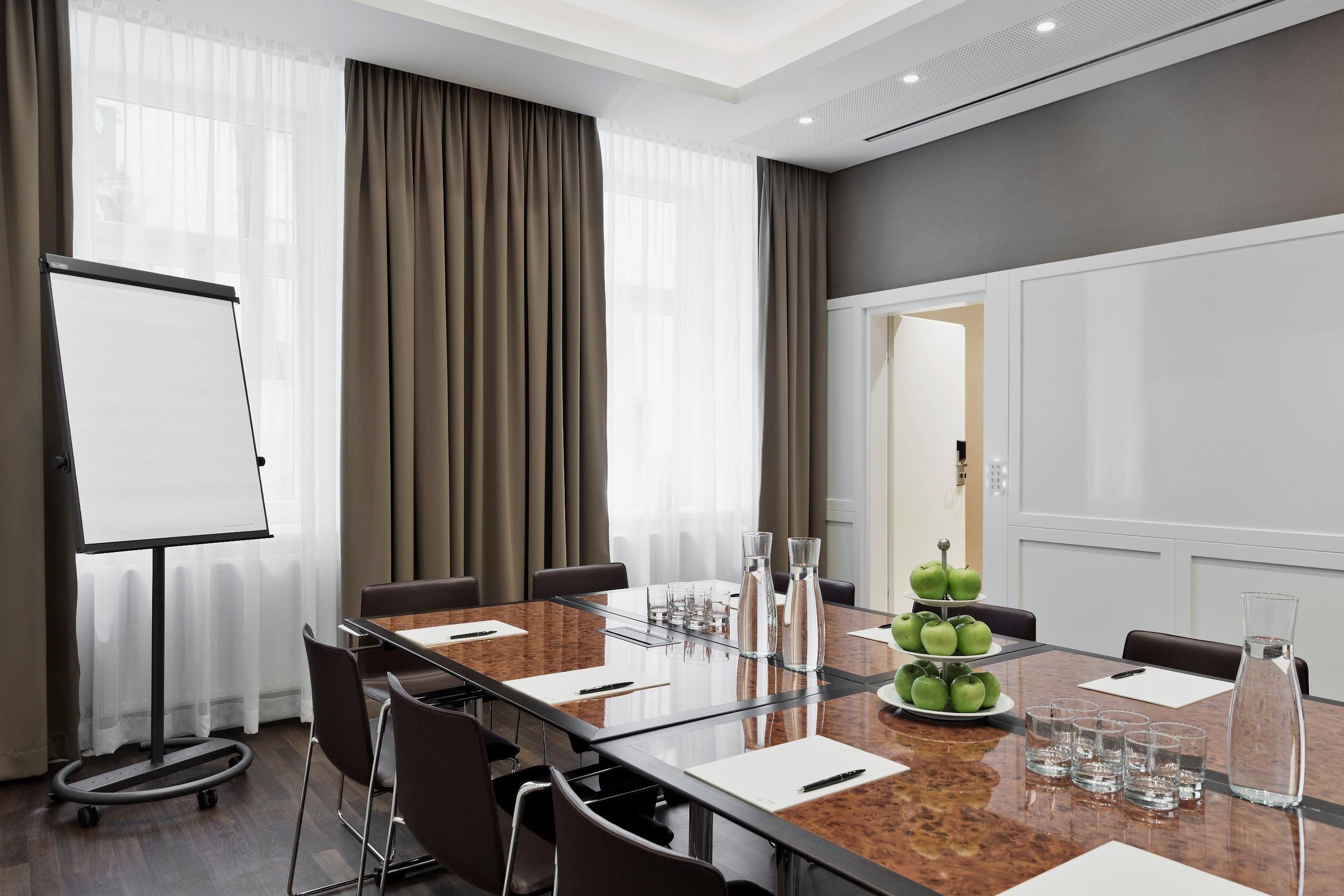 A conference room with a glass table, chairs, a whiteboard, and a door leading to another room.