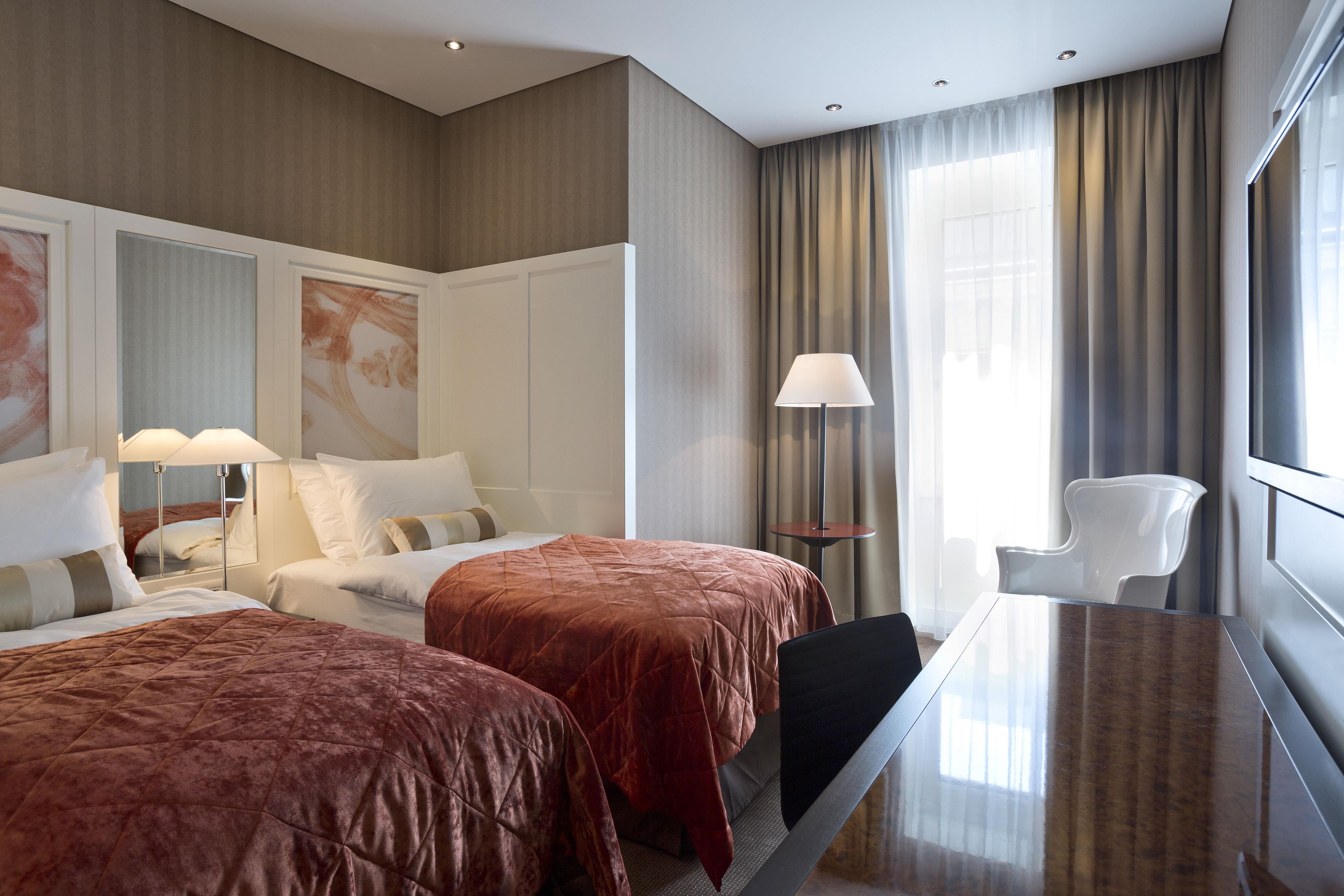 Ett hotellrum med två sängar, ett skrivbord, en stol och ett stort fönster med gardiner.