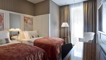 Ett hotellrum med två sängar, ett skrivbord, en stol och ett stort fönster med gardiner.