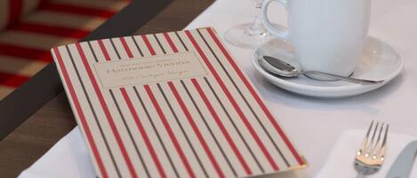 Una mesa ordenada con un menú, una taza blanca, una cuchara y un tenedor.
