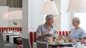 Un comedor con asientos tipo cabina a rayas rojas y blancas, mesas blancas y lámparas colgantes.