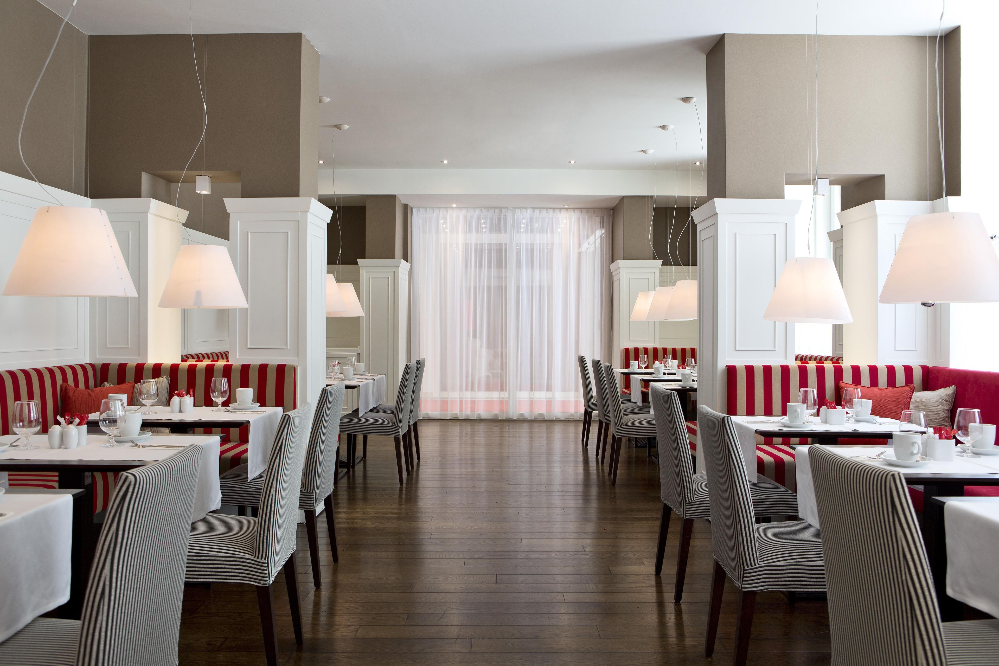 Ein Restaurant mit gestreiften Sitzecken und Tischen, weißen Lampen und einem Holzboden.