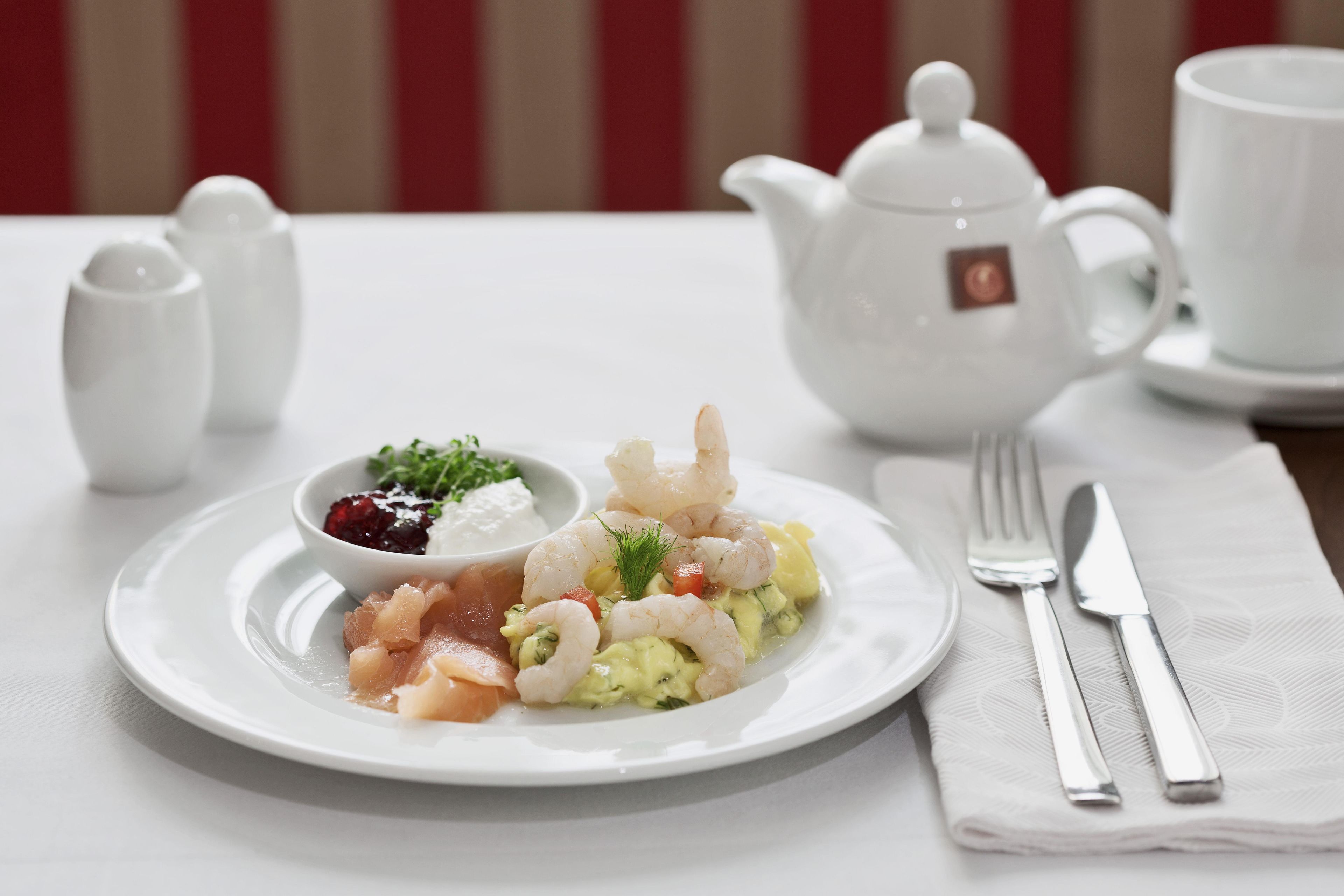 A white table setting with a plate of food, a teapot, cups, and cutlery.