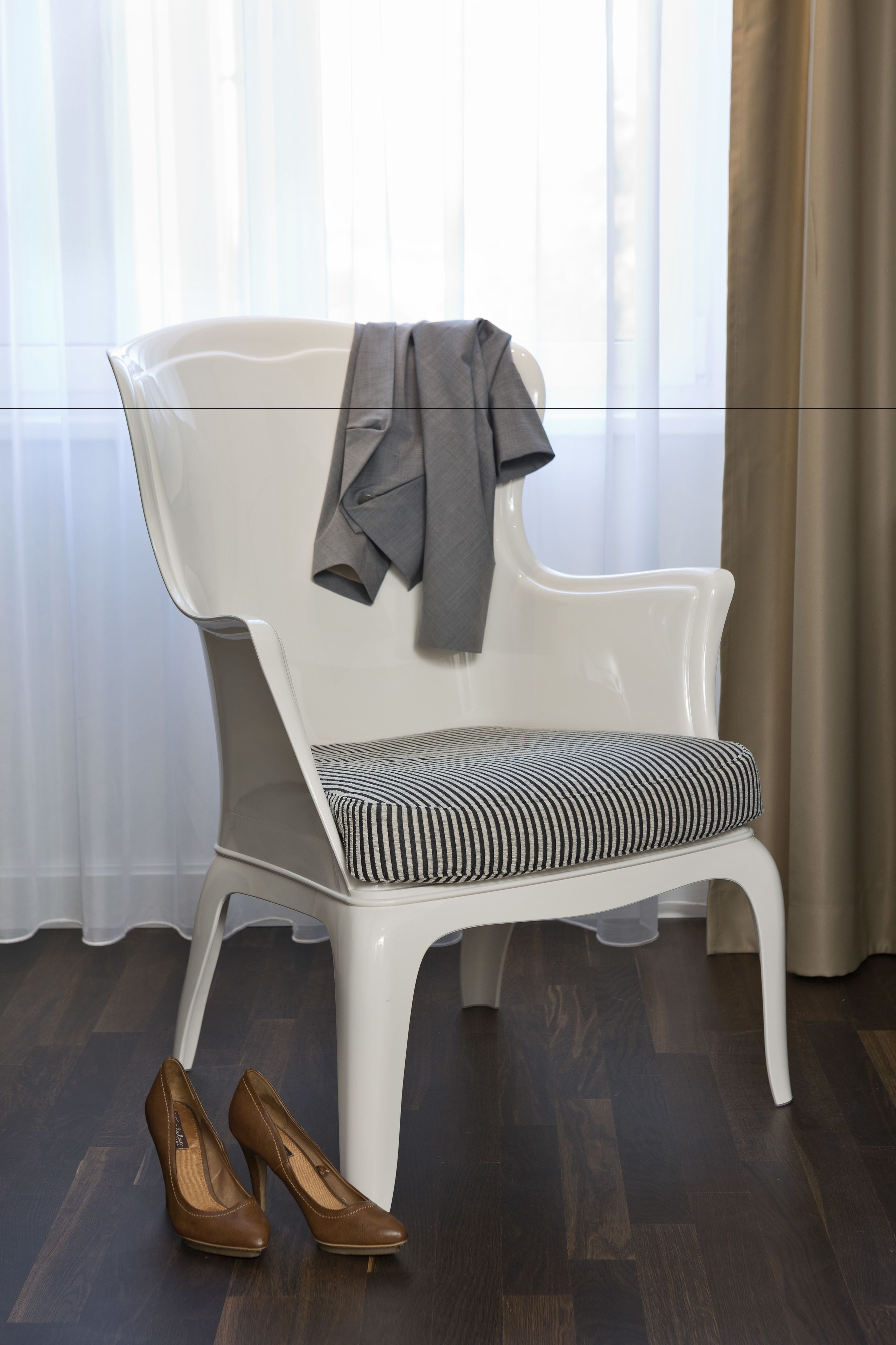 Una silla blanca con un cojín a rayas y una chaqueta gris colgada sobre ella.