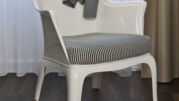A white chair with a striped cushion and a grey jacket draped over it. A pair of brown high-heeled shoes is placed on the floor beside the chair.