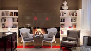 A modern living room with a fireplace, two white armchairs, a glass coffee table, and a bookshelf filled with books. - The Harmonie Vienna, BW Premier Collection (Vienna)