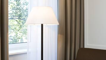 Habitación de hotel con una mesa, una lámpara, un sofá y vistas a árboles a través de cortinas traslúcidas.