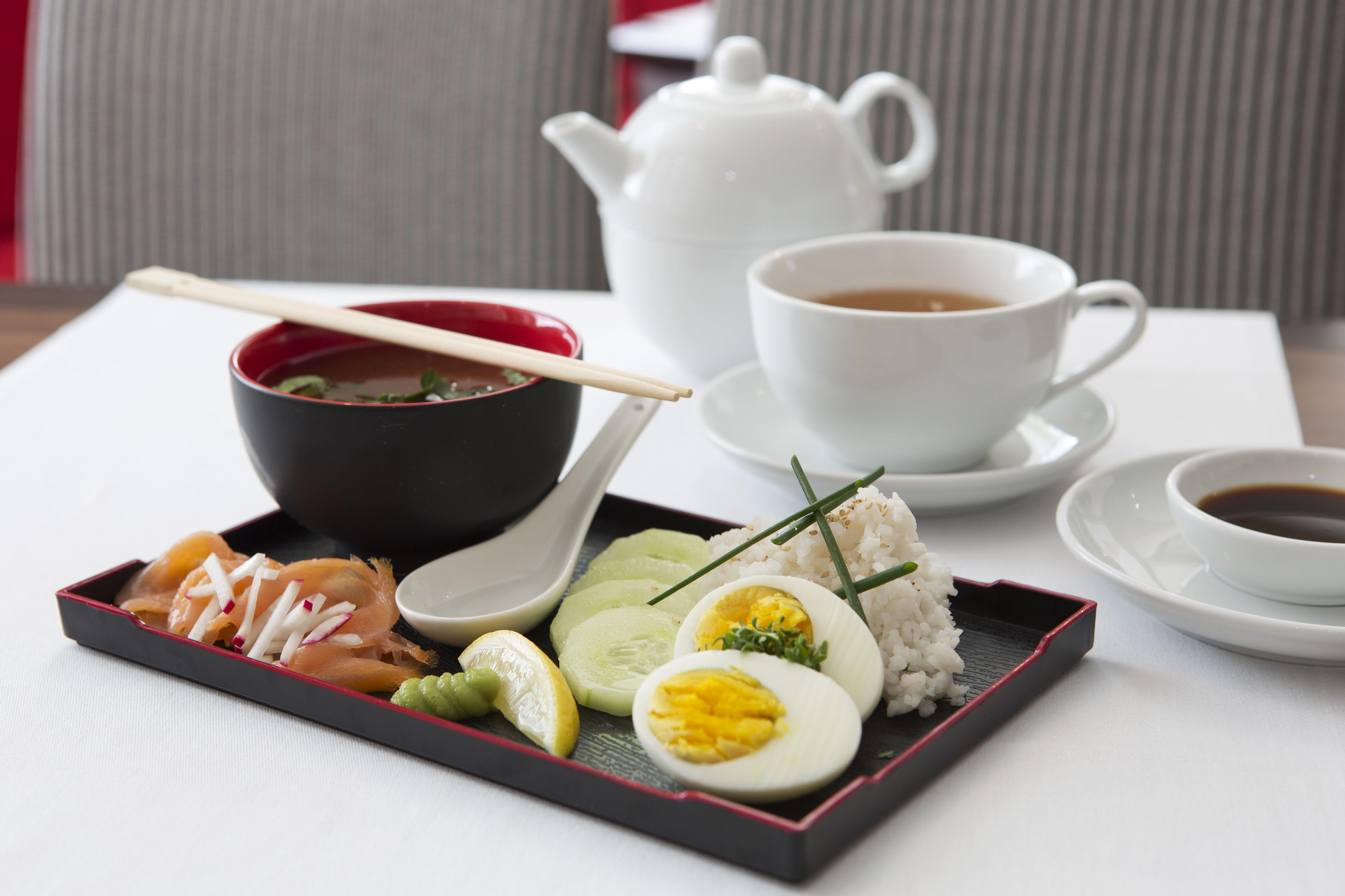 Una comida tradicional japonesa con un calentador de té, una taza de té y una bandeja con sashimi, arroz, huevo y encurtidos.