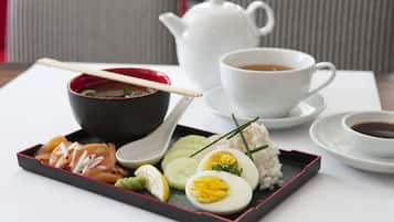 Una comida tradicional japonesa con un calentador de té, una taza de té y una bandeja con sashimi, arroz, huevo y encurtidos.