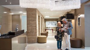 A modern hotel lobby with a reception desk, seating areas, and a large chandelier. - The Harmonie Vienna, BW Premier Collection (Vienna)