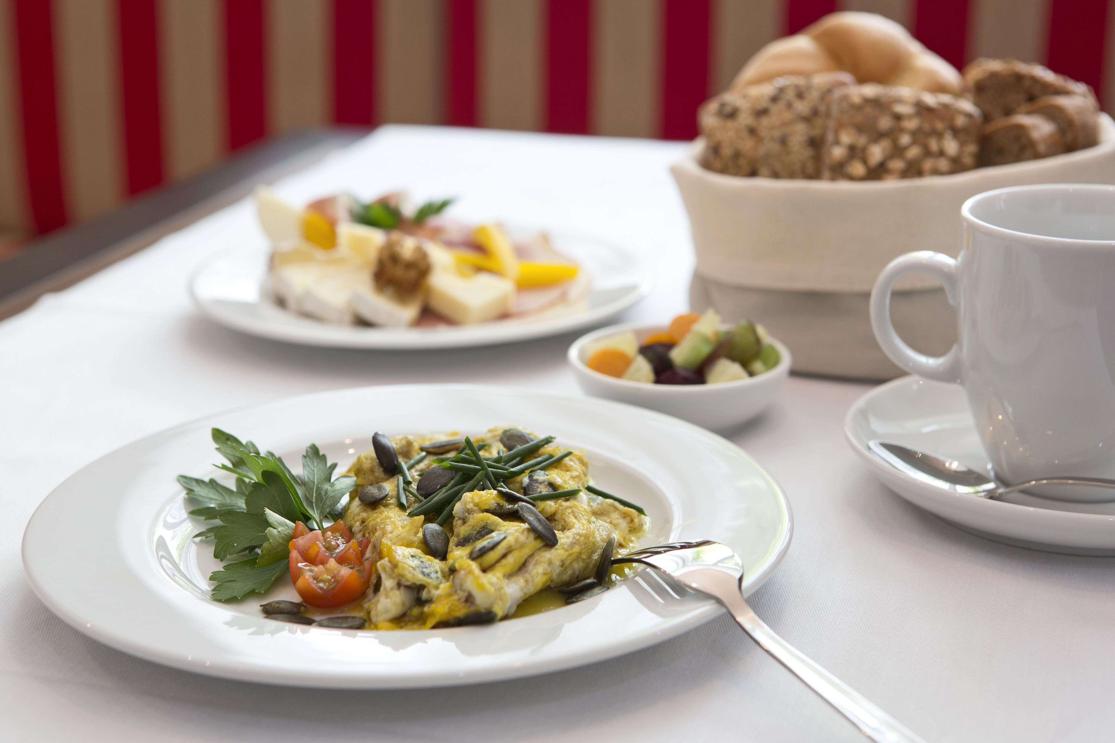 A breakfast setting with plates of food, a cup, and a bowl of bread.