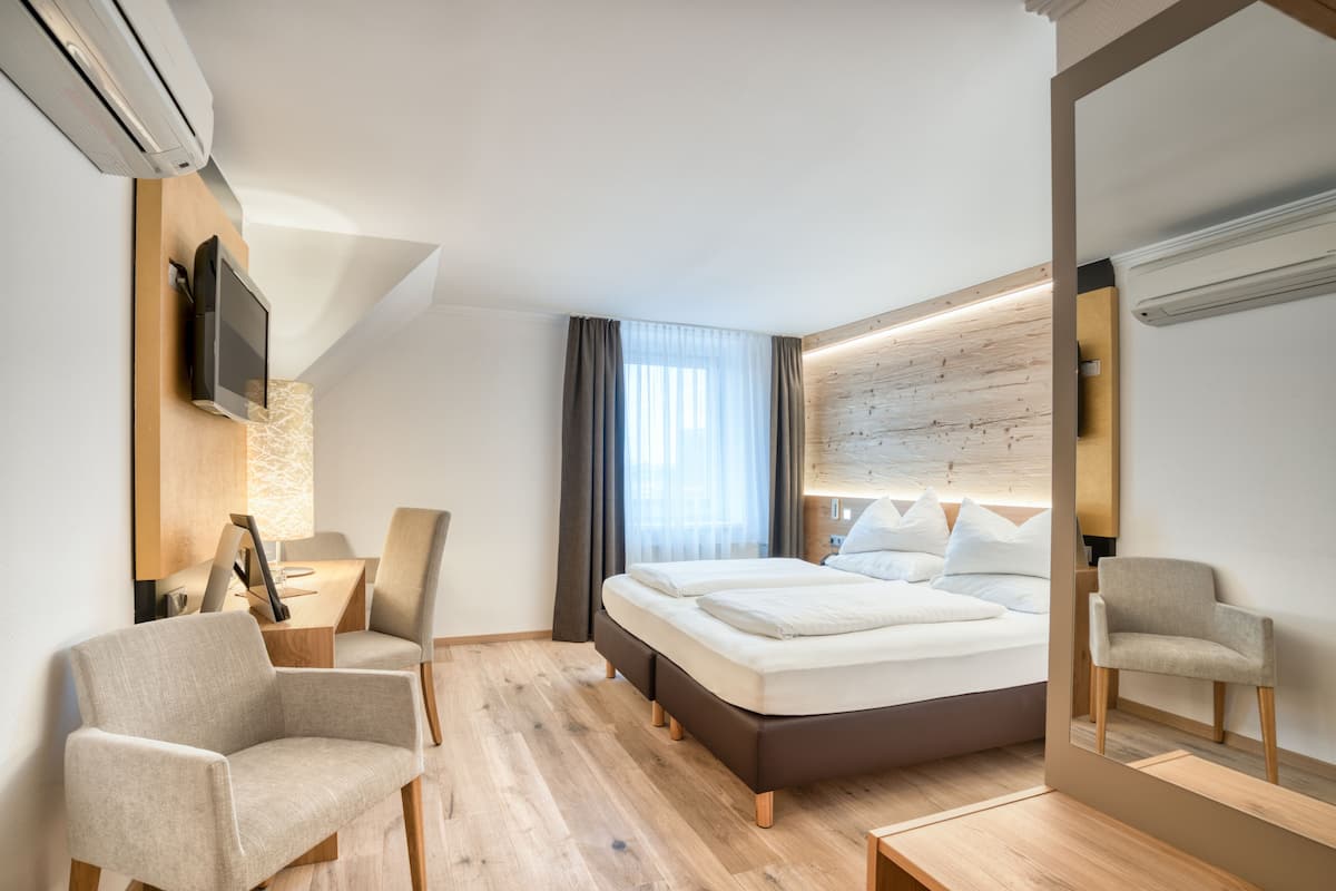 A modern hotel room with a bed, a desk with a chair, a TV, and a large mirror.