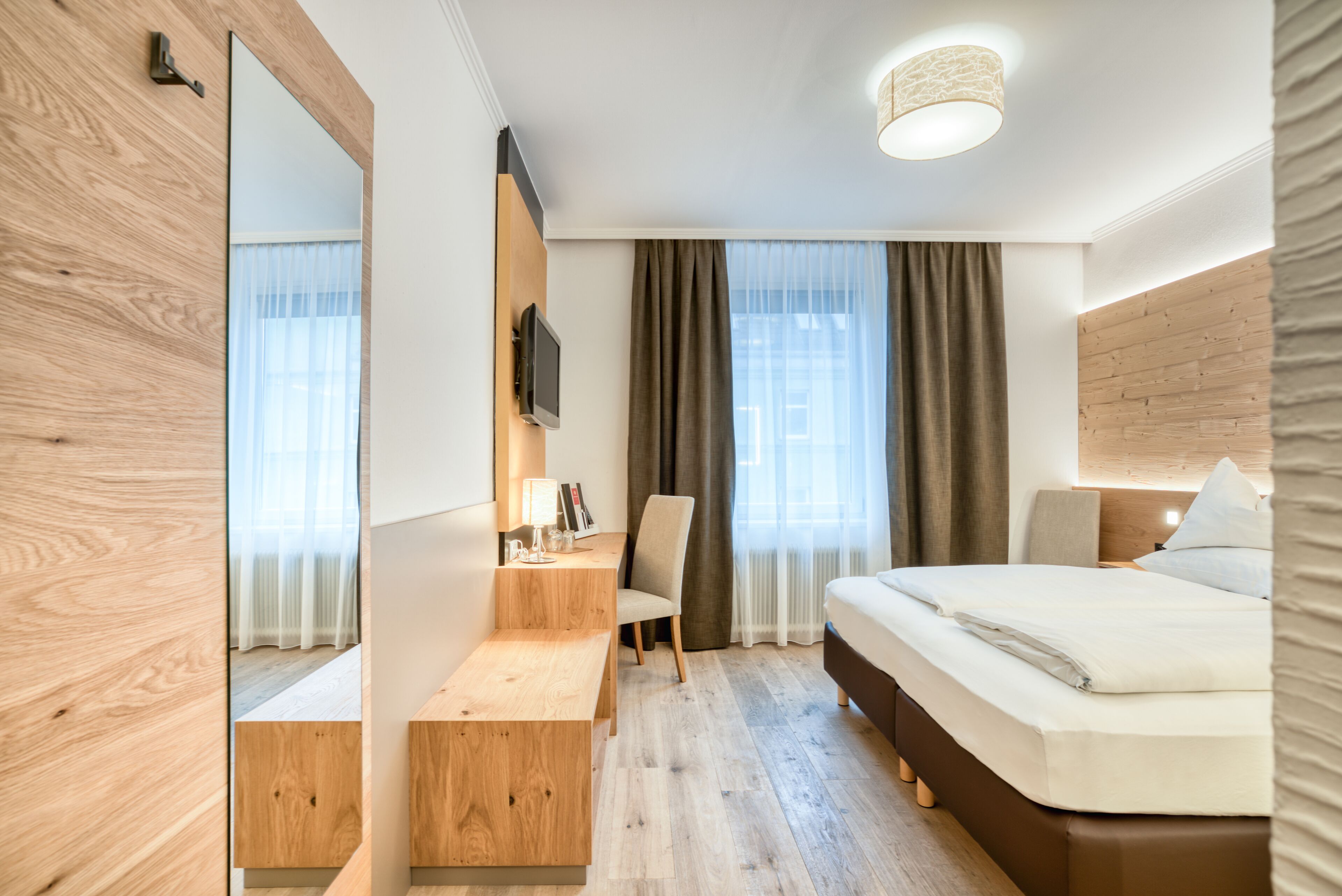Ett modernt hotellrum med trägolv, en säng, ett skrivbord och en stol.