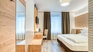 Ett modernt hotellrum med trägolv, en säng, ett skrivbord och en stol.