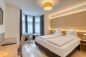 A modern hotel room with a large bed, a desk, and a chair.