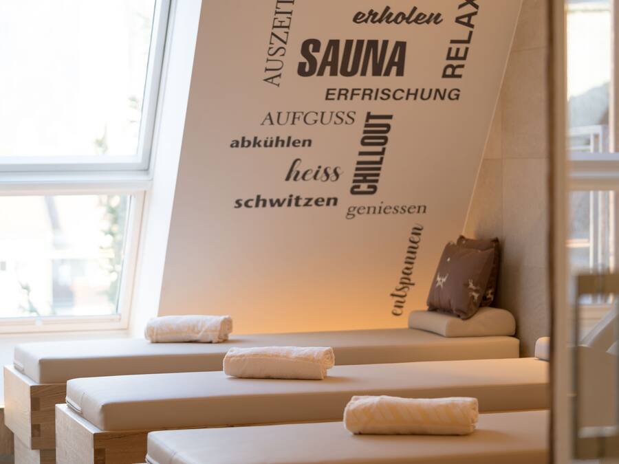A spa room with a wall featuring words like "SAUNA," "CHILLOUT," and "RELAX." There are two massage tables with towels.