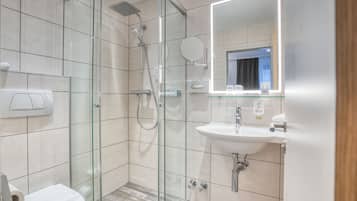 Une salle de bain moderne avec une douche à parois de verre, un lavabo blanc et un miroir doté d’un cadre éclairé.