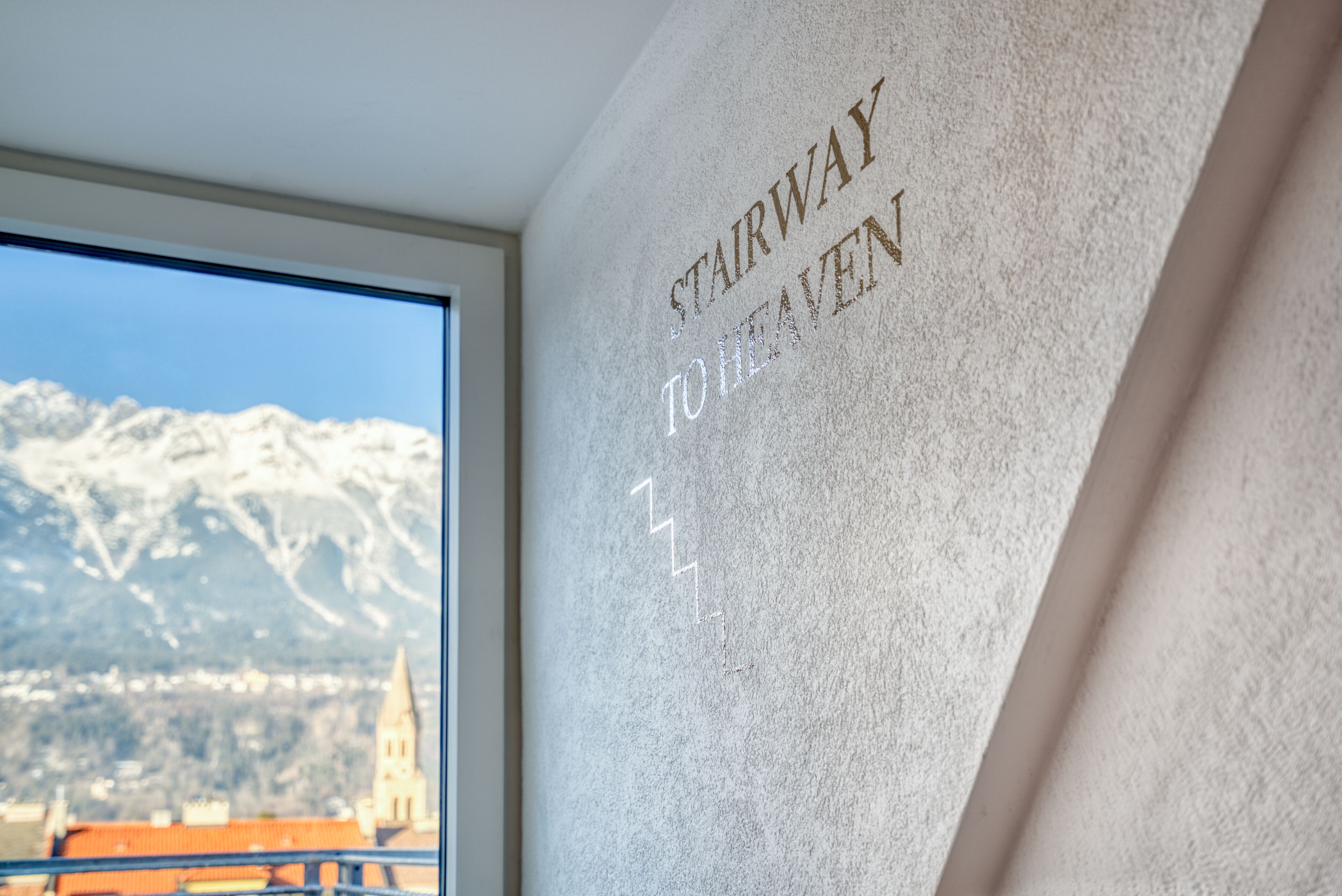 A wall with the inscription "STAIRWAY TO HEAVEN" and a view of snow-capped mountains through a window.
