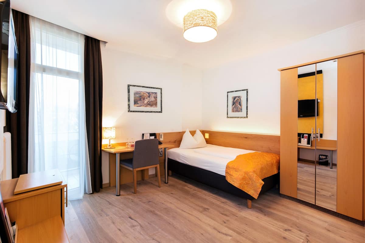 A hotel room with a bed, desk, chair, wardrobe, and two framed pictures on the wall.