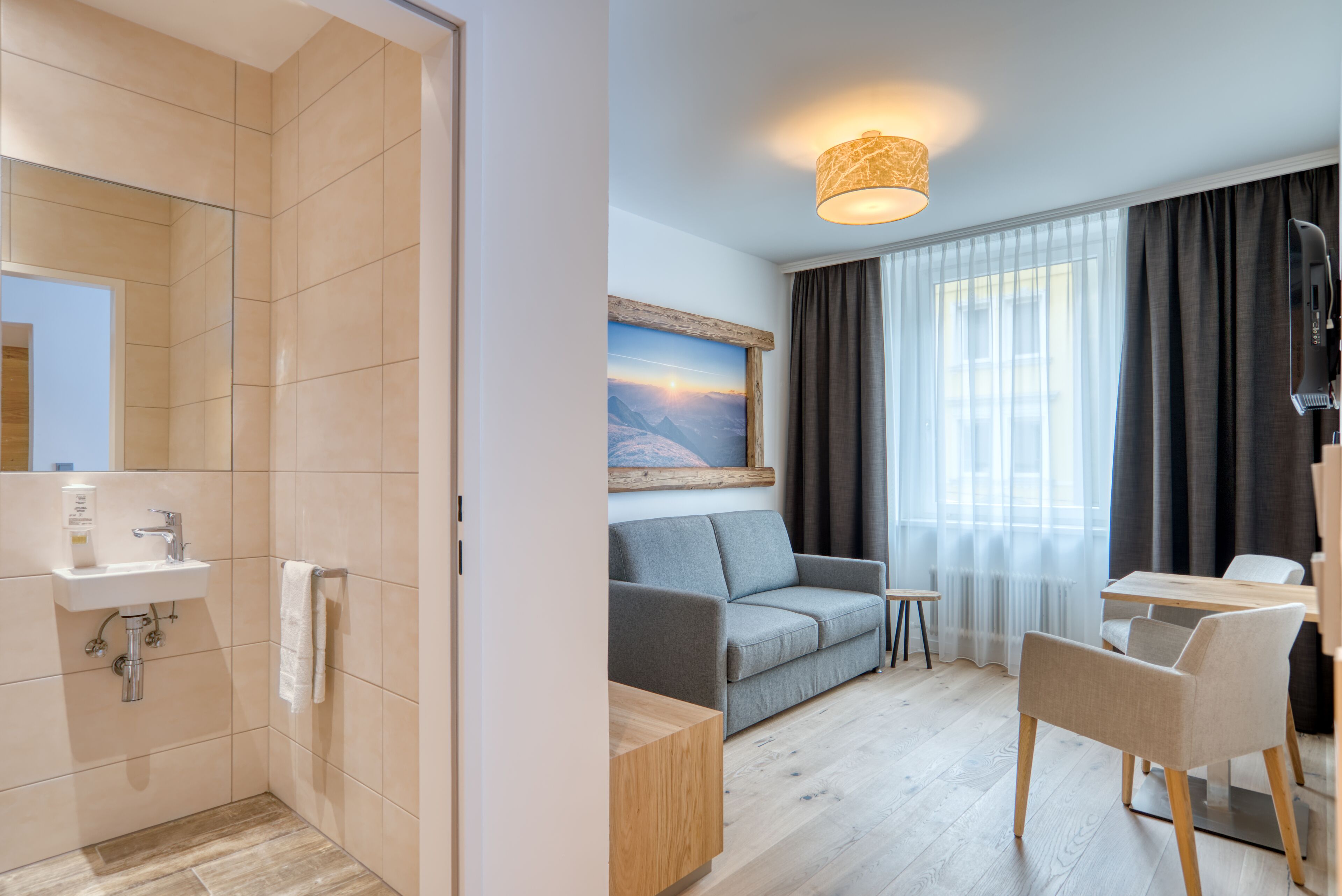 Una habitación de hotel moderna con ducha, lavamanos y un área de estar con sofá y sillones.